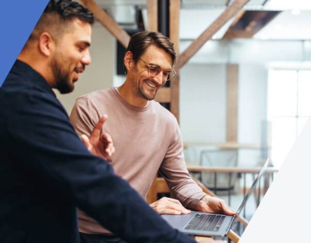 Zwei Männer unterhalten sich fröhlich und schauen auf ihre Laptops – zeigt kollaboratives und zuverlässiges Shop-Hosting für erfolgreiche Online-Businesses.